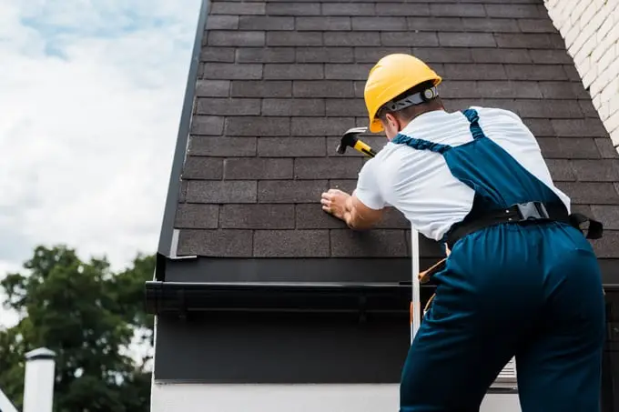 Roofer fastening asphalt shingles along the edge of a Calgary roof