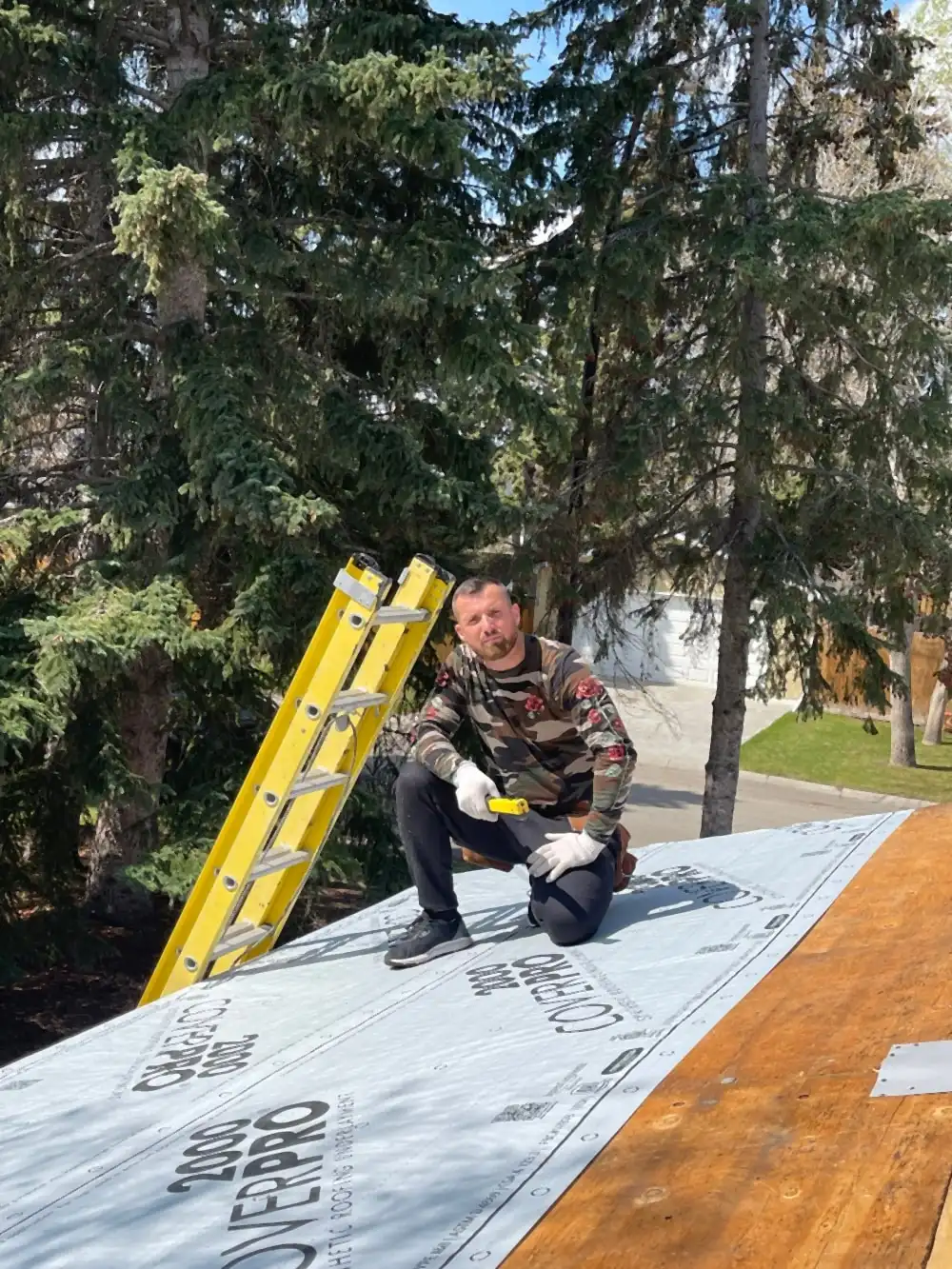 Pashk Vukaj, founder of Calgary Roof Repair Ltd, kneeling on a Calgary roof deck with new underlayment laid down